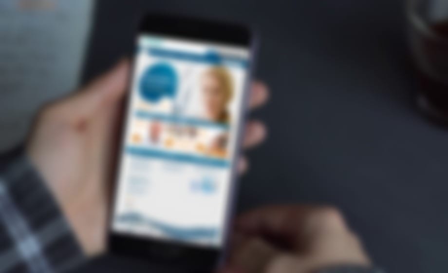 Hand holding a phone showing a healthcare website scaled to the small screen
